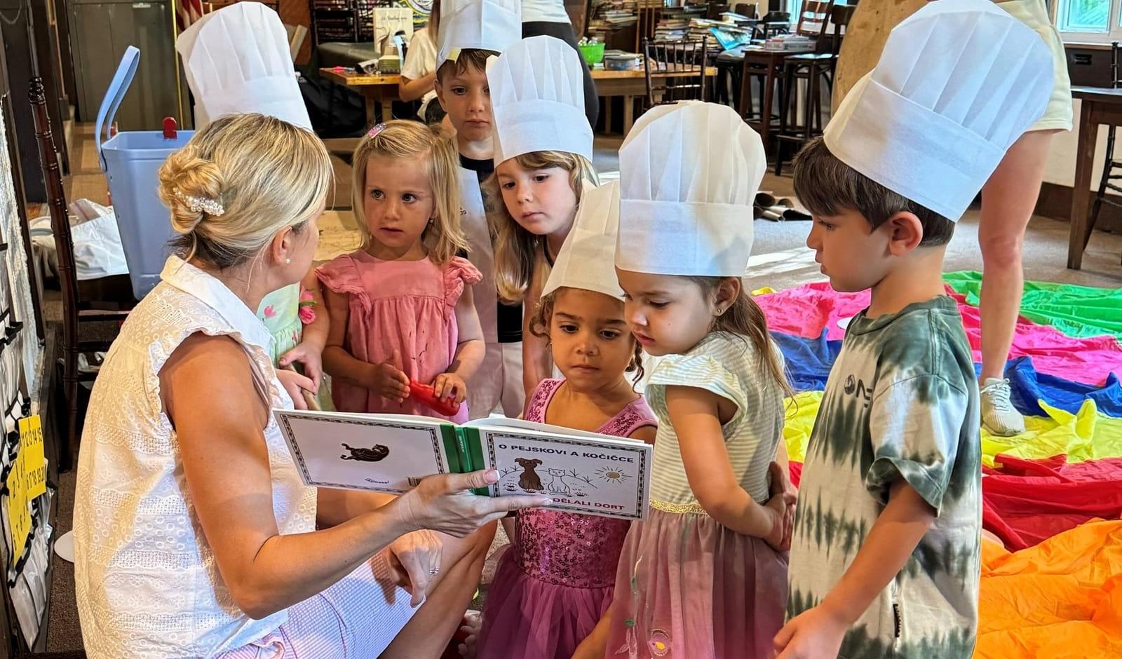 A teacher reading a Czech picture book to children in paper chef hats