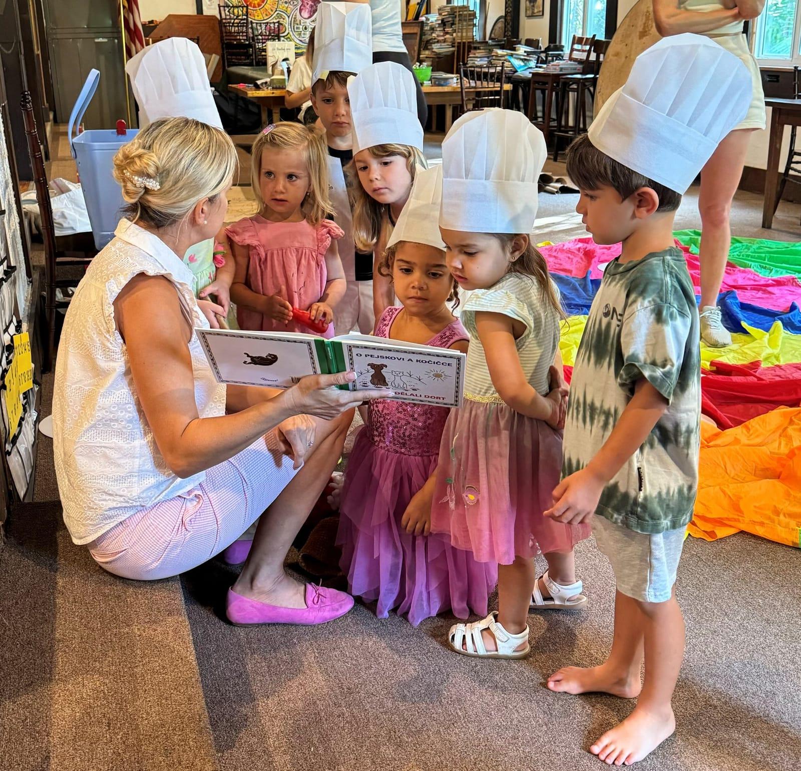 A teacher reading a Czech picture book to children in paper chef hats
